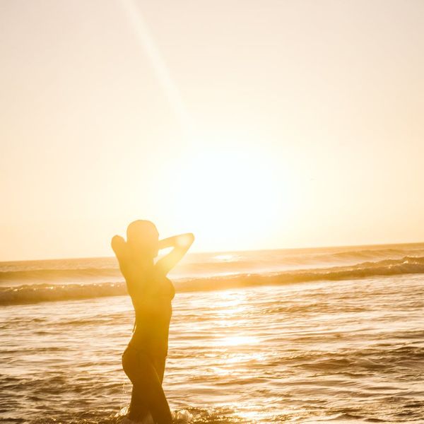 Person stretching outdoors during sunrise, silhouette against a bright sky.