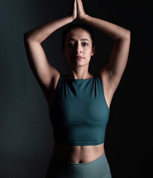 Woman in a calm yoga pose in a dark studio with cyan light.